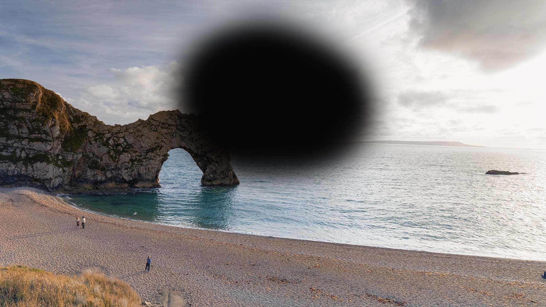 How someone with AMD might experience a view of Durdle Door - a large, blurred black shape covers the central part of the scene